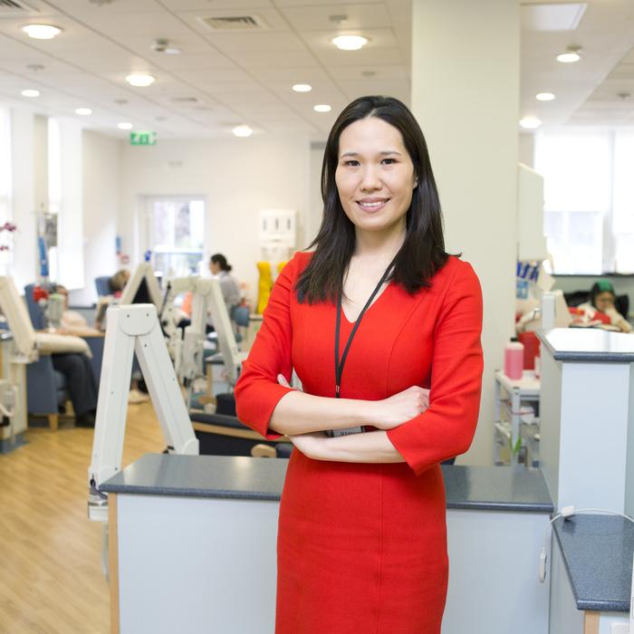 Irene Chong smiles as she stands in a treatment unit. She has long black hair and is wearing a red dress.